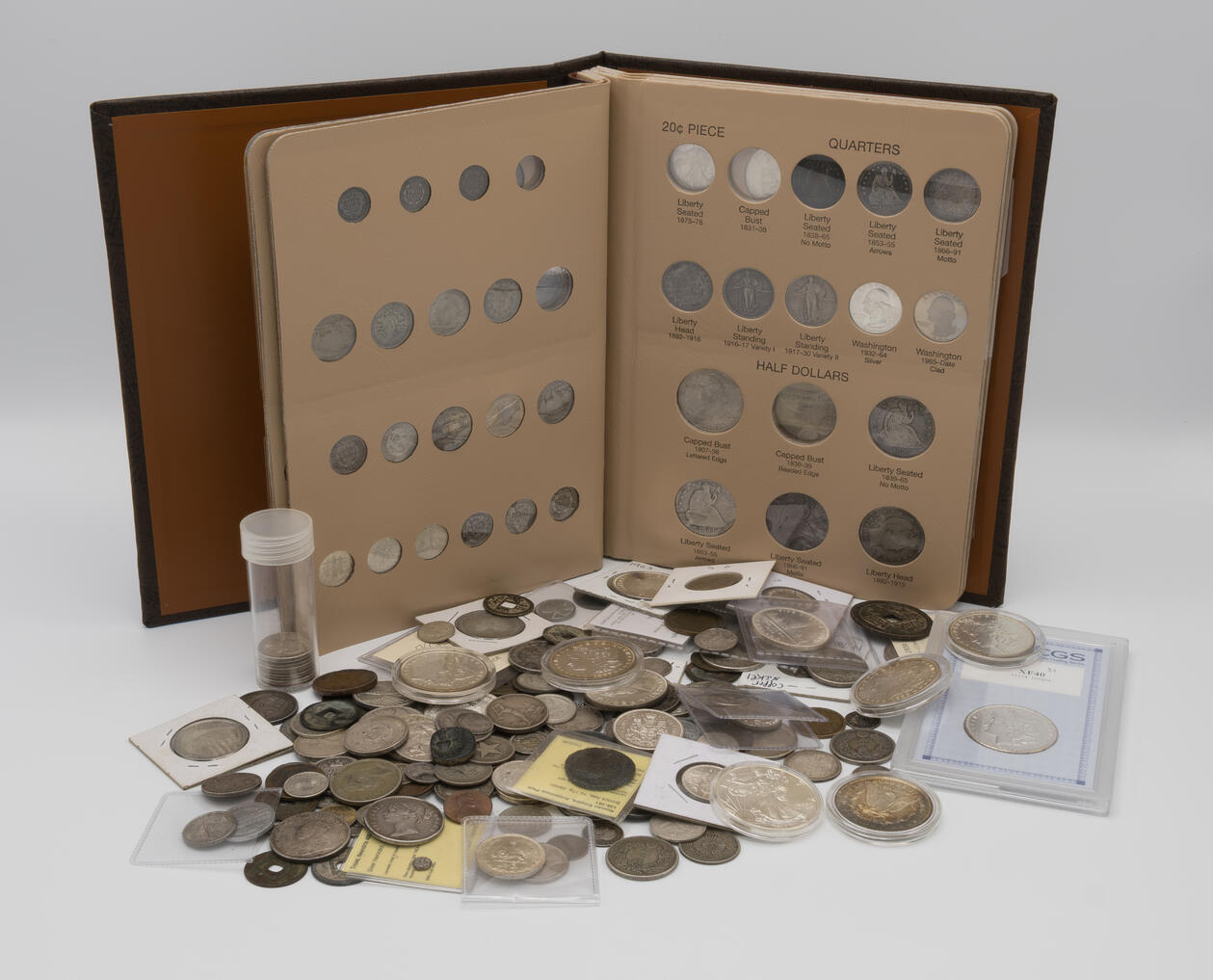 A coin album with a pile of coins in front of it, in various containers / sleeves.